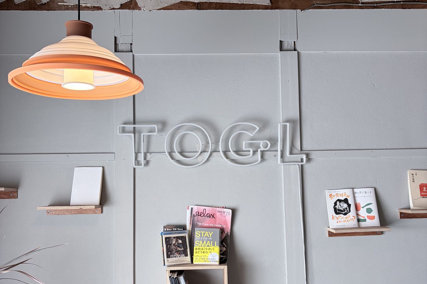 DIY BOOKSの店内。壁にTOGLのネオンサイン、ペンダントライトと本の並ぶ棚